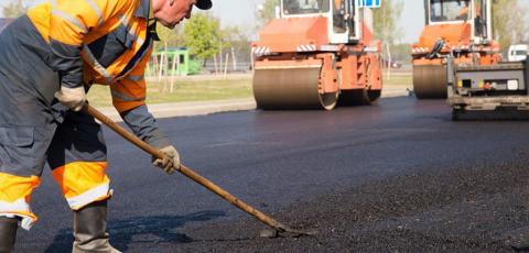 Man with reflective clothing evening out fresh asphalt with two roller machines in the background